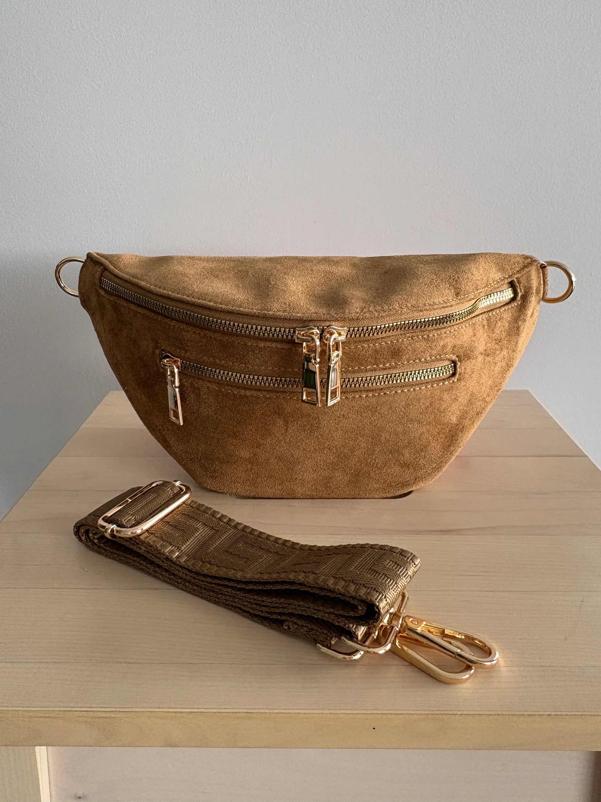 Sac banane toucher daim camel avec 2 poches zip doré et sangle fantaisie posé sur une table en bois
