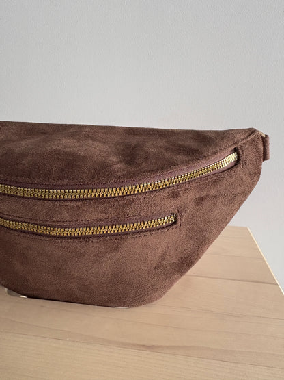 Sac banane toucher daim marron chocolat avec 2 poches zippées et détails dorés, posé sur une surface en bois