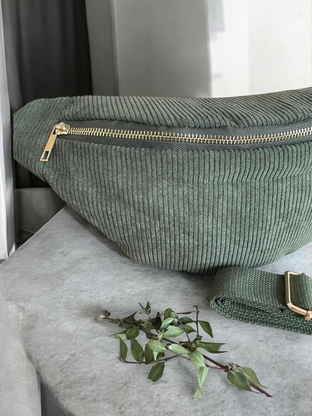 Green corduroy fanny pack with gold zipper on gray surface, trendy Le Petit Placard accessory