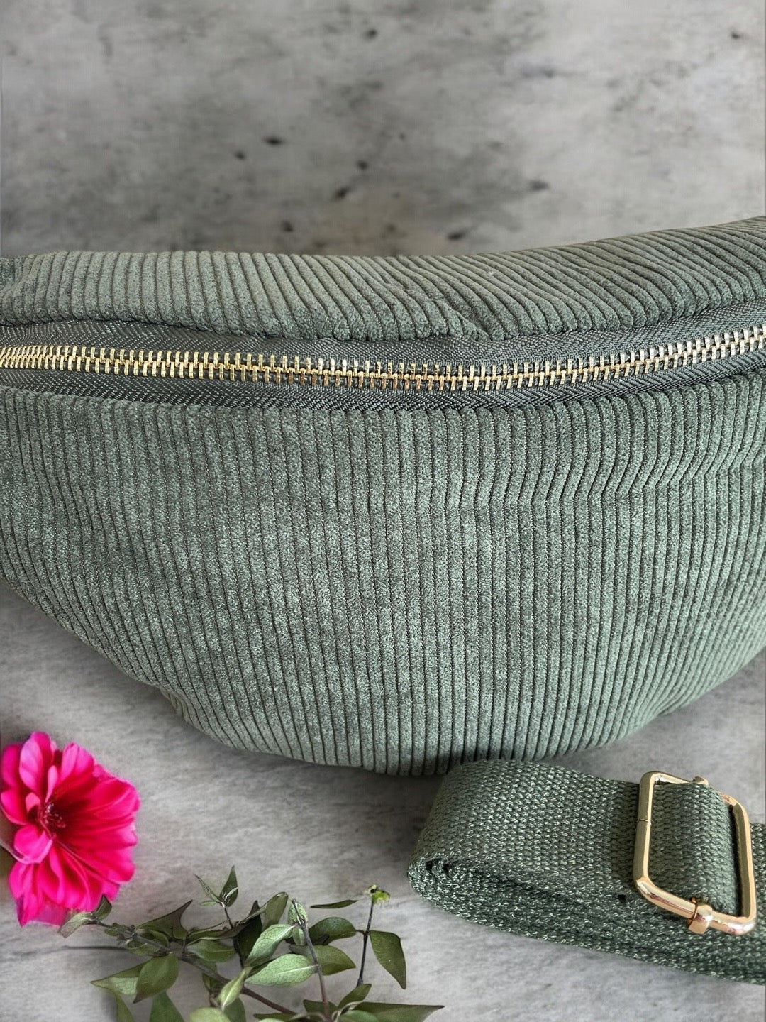 Green corduroy fanny pack with gold zipper, Le Petit Placard accessory, on stone surface