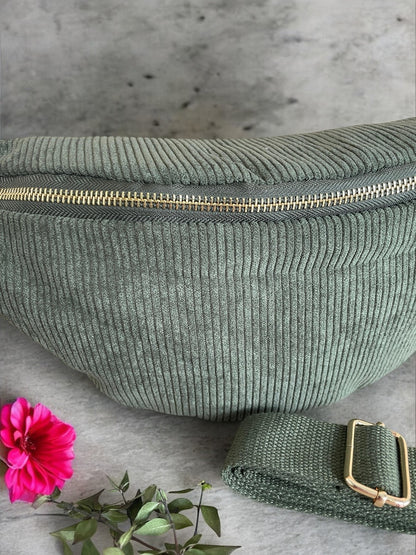 Green corduroy fanny pack with gold zipper, Le Petit Placard accessory, on stone surface
