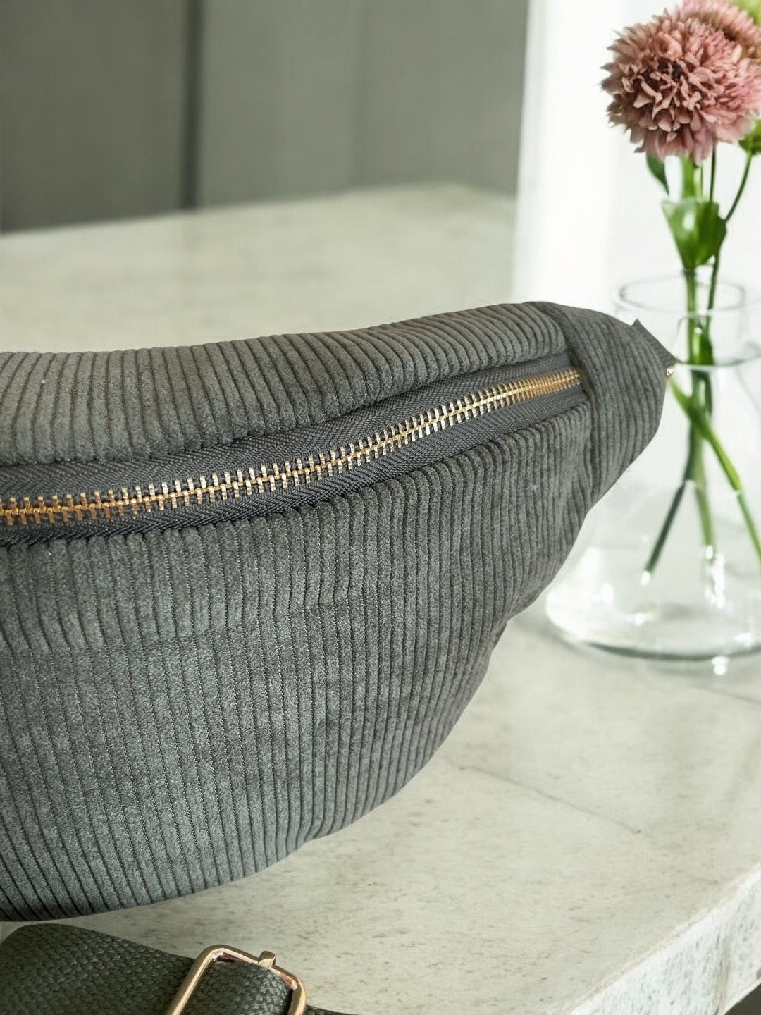 Grey corduroy belt bag with gold zipper from Le Petit Placard, styled on marble table