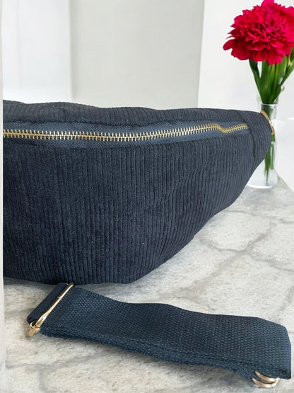 Black textured sac banane with gold zipper on marble surface, red flower in background