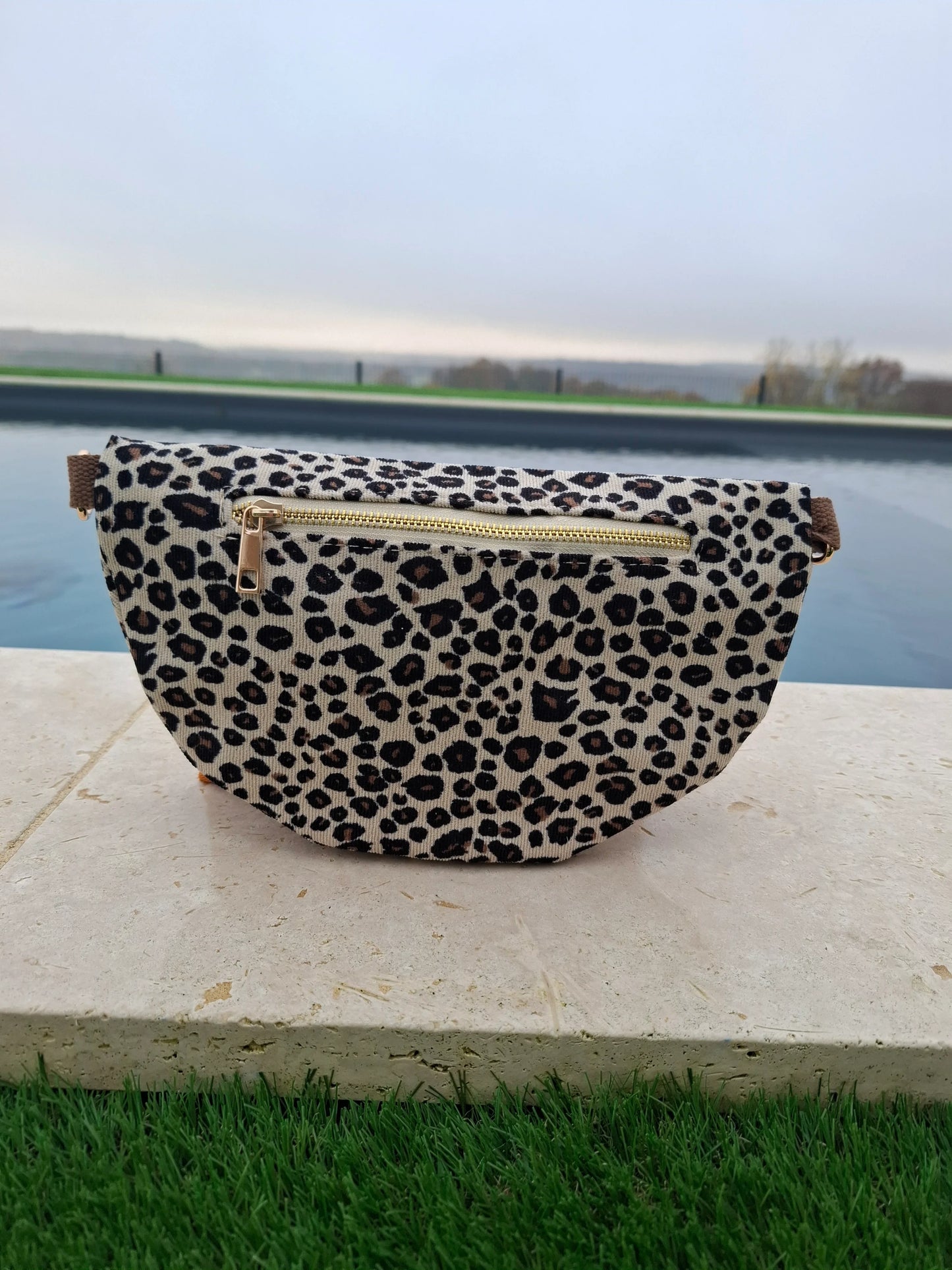 Sac banane velours côtelé imprimé léopard beige et noir avec fermeture éclair dorée, posé en extérieur