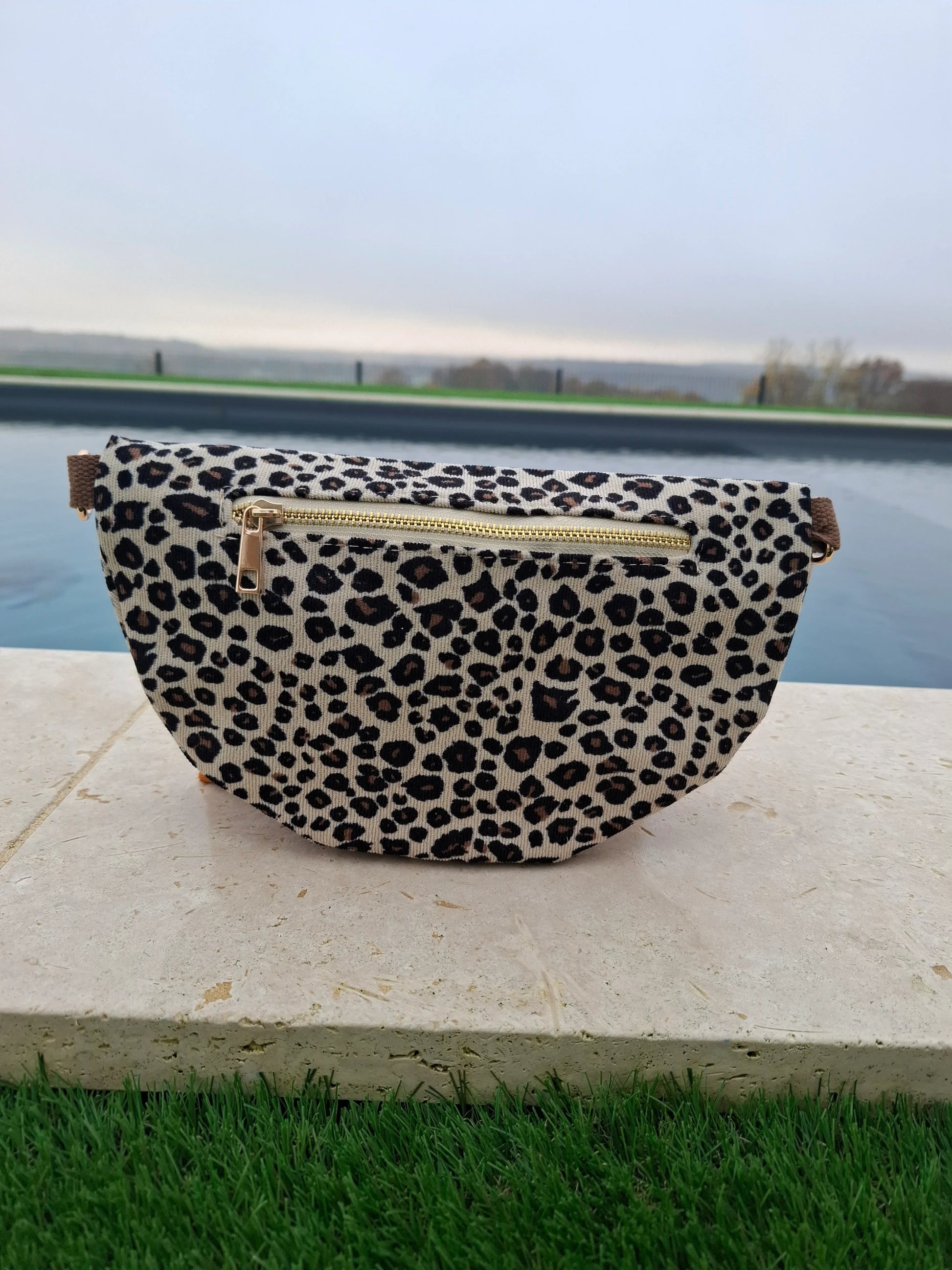 Sac banane velours côtelé imprimé léopard beige et noir avec fermeture éclair dorée, posé en extérieur