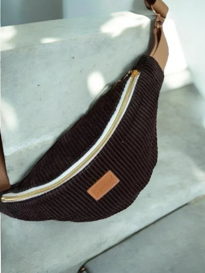 Brown corduroy bum bag with beige strap and zipper, displayed on a concrete step, Le Petit Placard