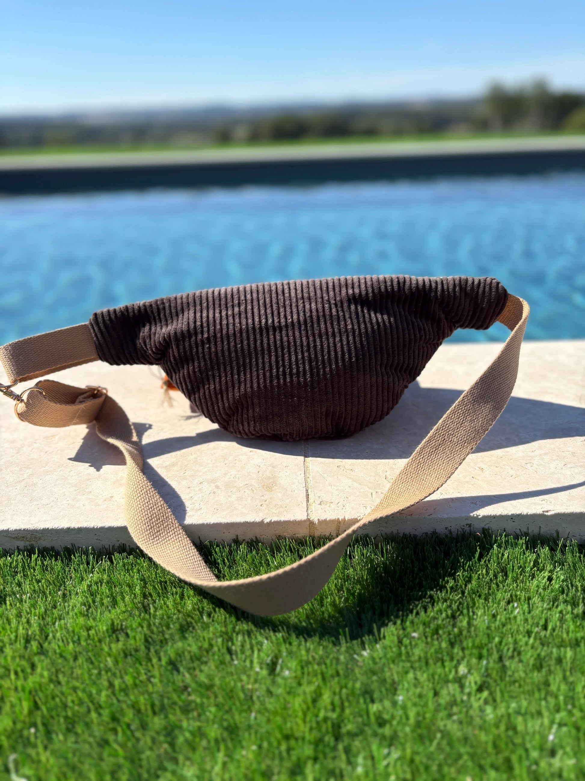 Brown corduroy fanny pack with beige strap by a pool, trendy accessory from Le Petit Placard