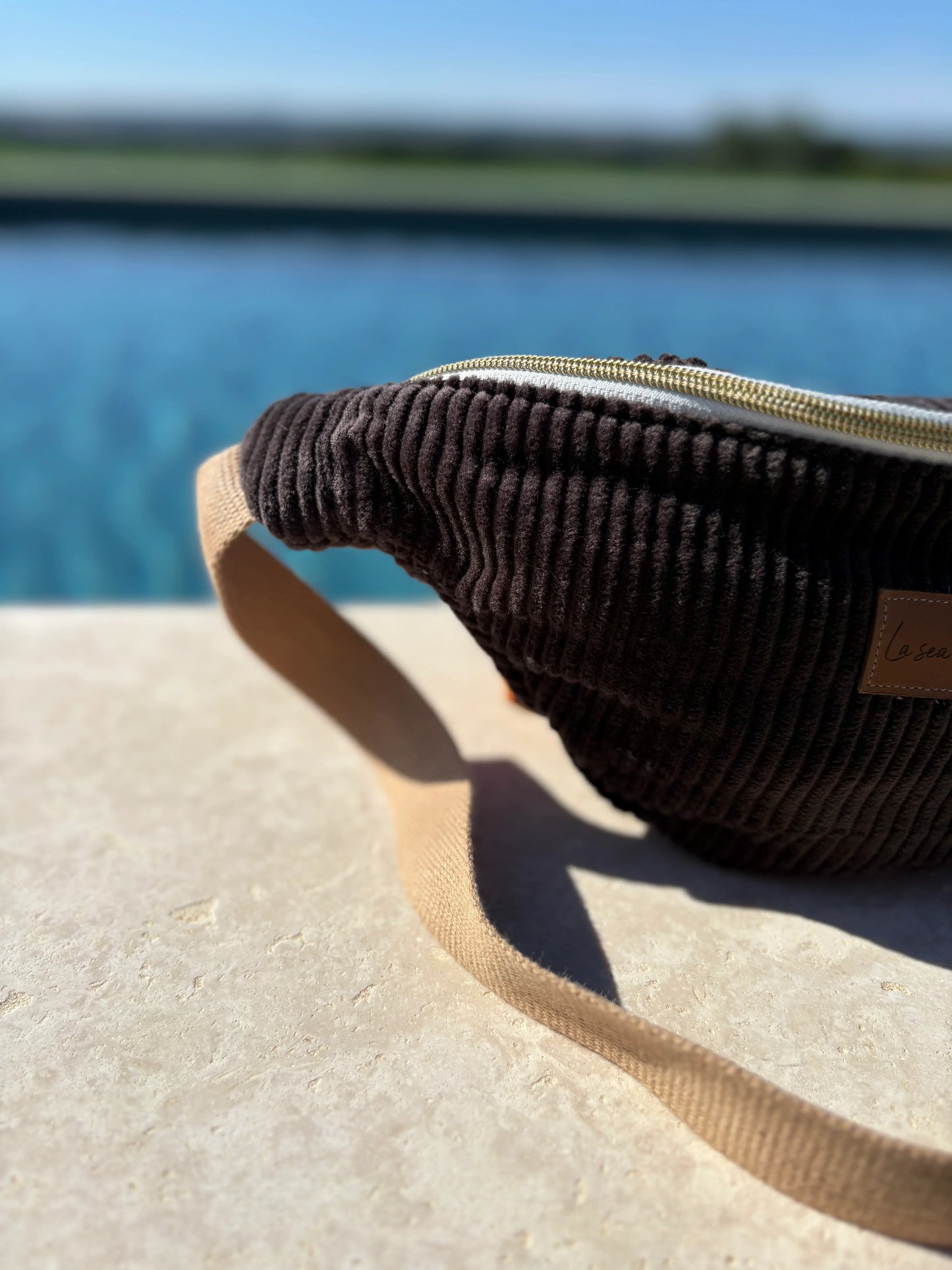 Corduroy brown sac banane by a poolside, trendy accessory from Le Petit Placard