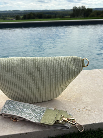 Sac banane velours côtelé vert d'eau avec anneau doré et sangle fantaisie motif losanges, posé au bord d'une piscine