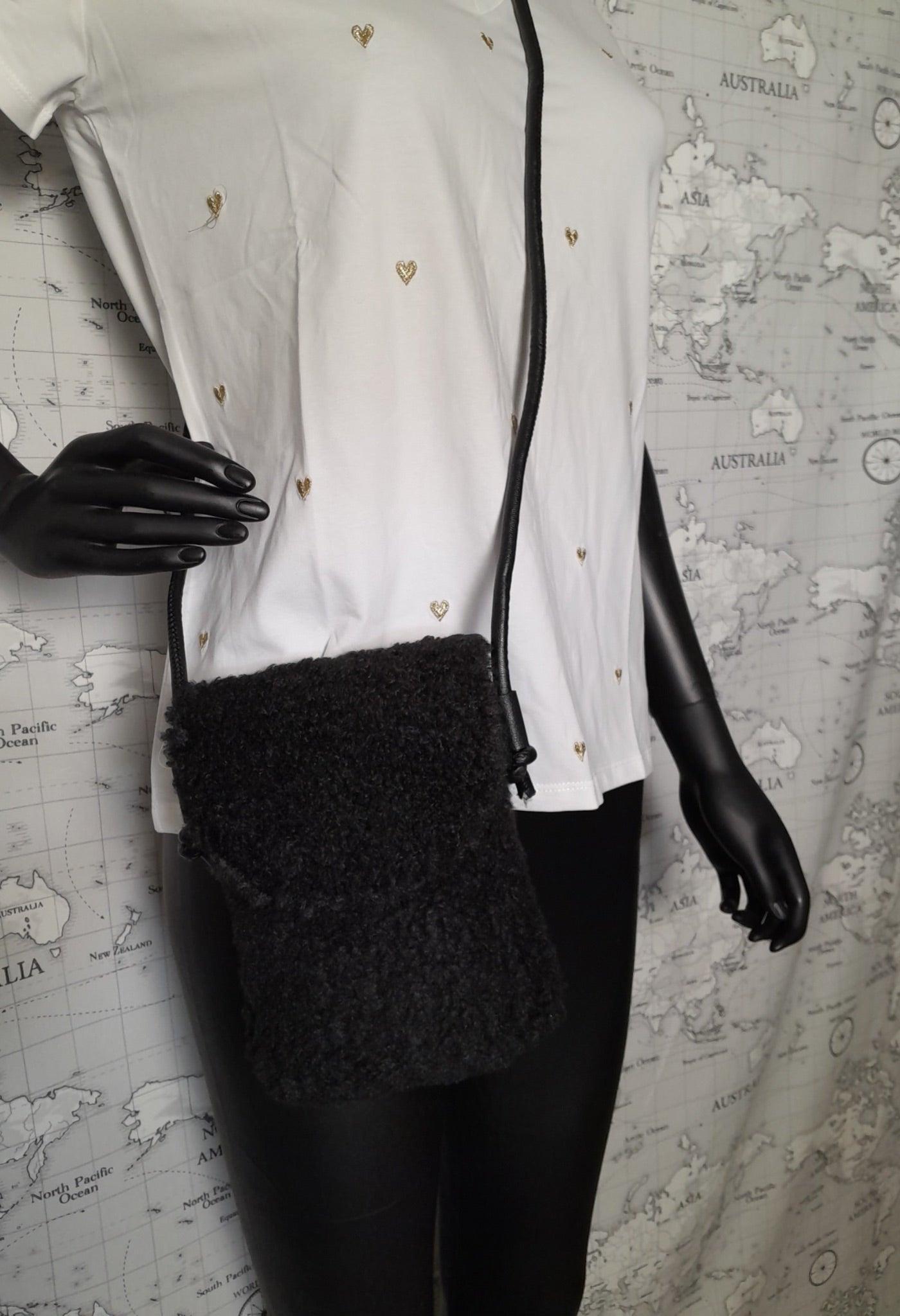 Black faux fur crossbody pouch bag with shoulder strap, displayed on mannequin in white shirt.