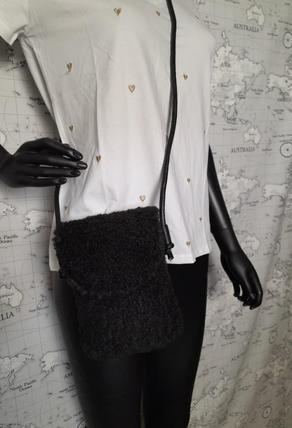 Black faux fur crossbody pouch bag with shoulder strap, displayed on mannequin in white shirt.