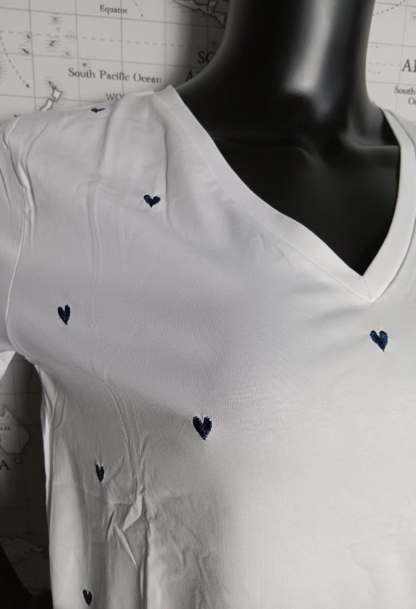 T-shirt blanc avec v avec des cœurs bleu marine brodés, en V-neck près du col, displayed sur un mannequin.