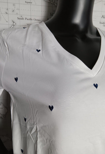 T-shirt blanc avec v avec des cœurs bleu marine brodés, en V-neck près du col, displayed sur un mannequin.