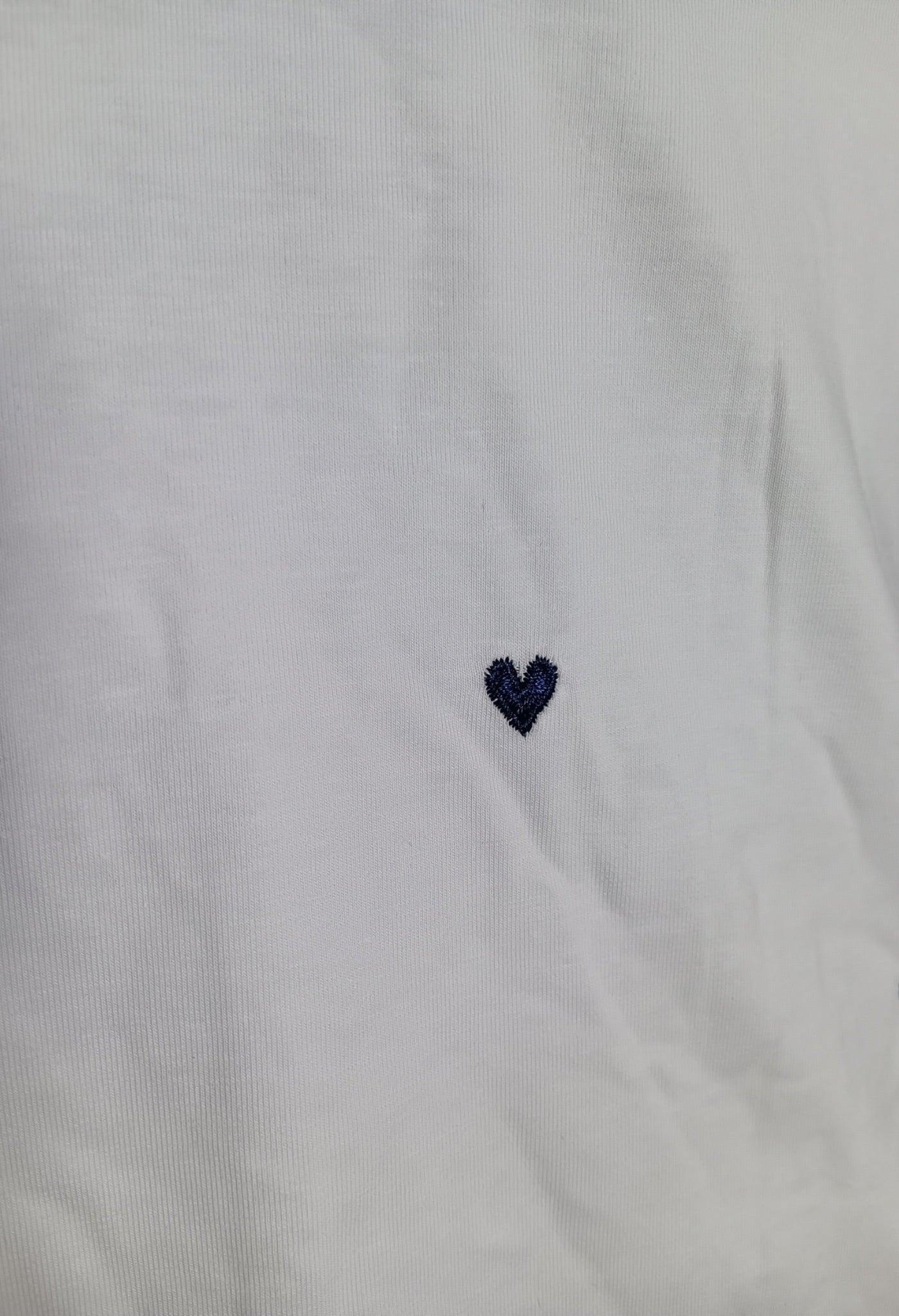Petit T-shirt blanc avec un petit cœur brodé bleu marine sur la poitrine.