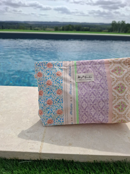 Trousse en tissu imperméabilisé patchwork fleuri rose bleu lavande, posée au bord d'une piscine