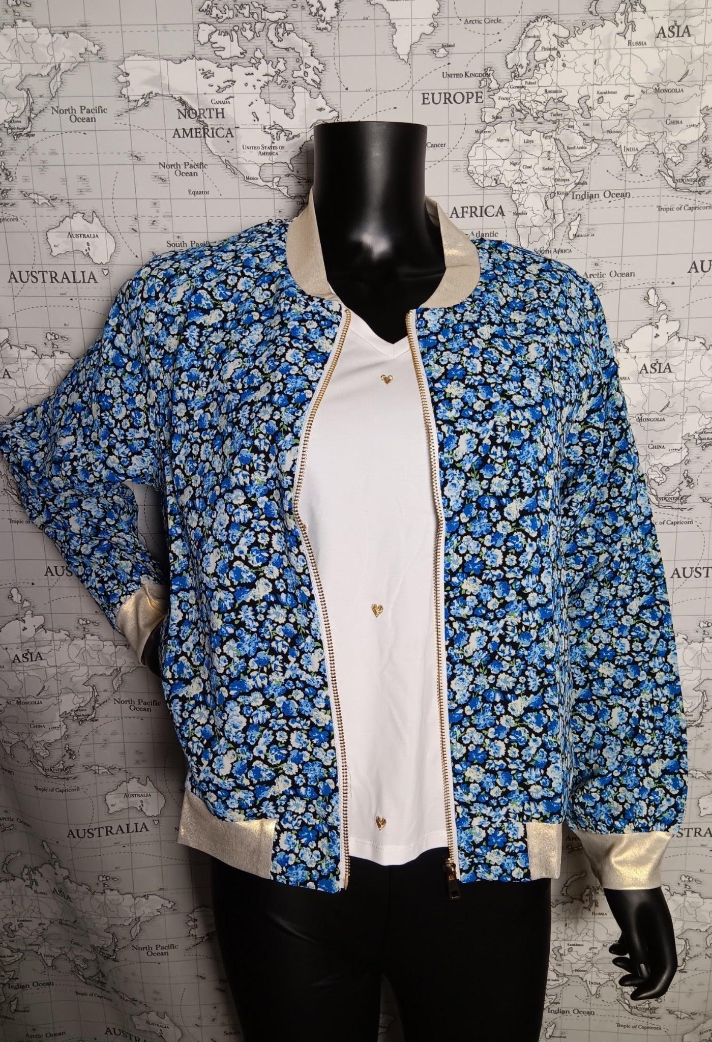 Veste bomber fleurie bleu femme, fermée par zip, sur mannequin noir, fond carte du monde. Le bomber offre motifs bleus, bordures et poignets crème.