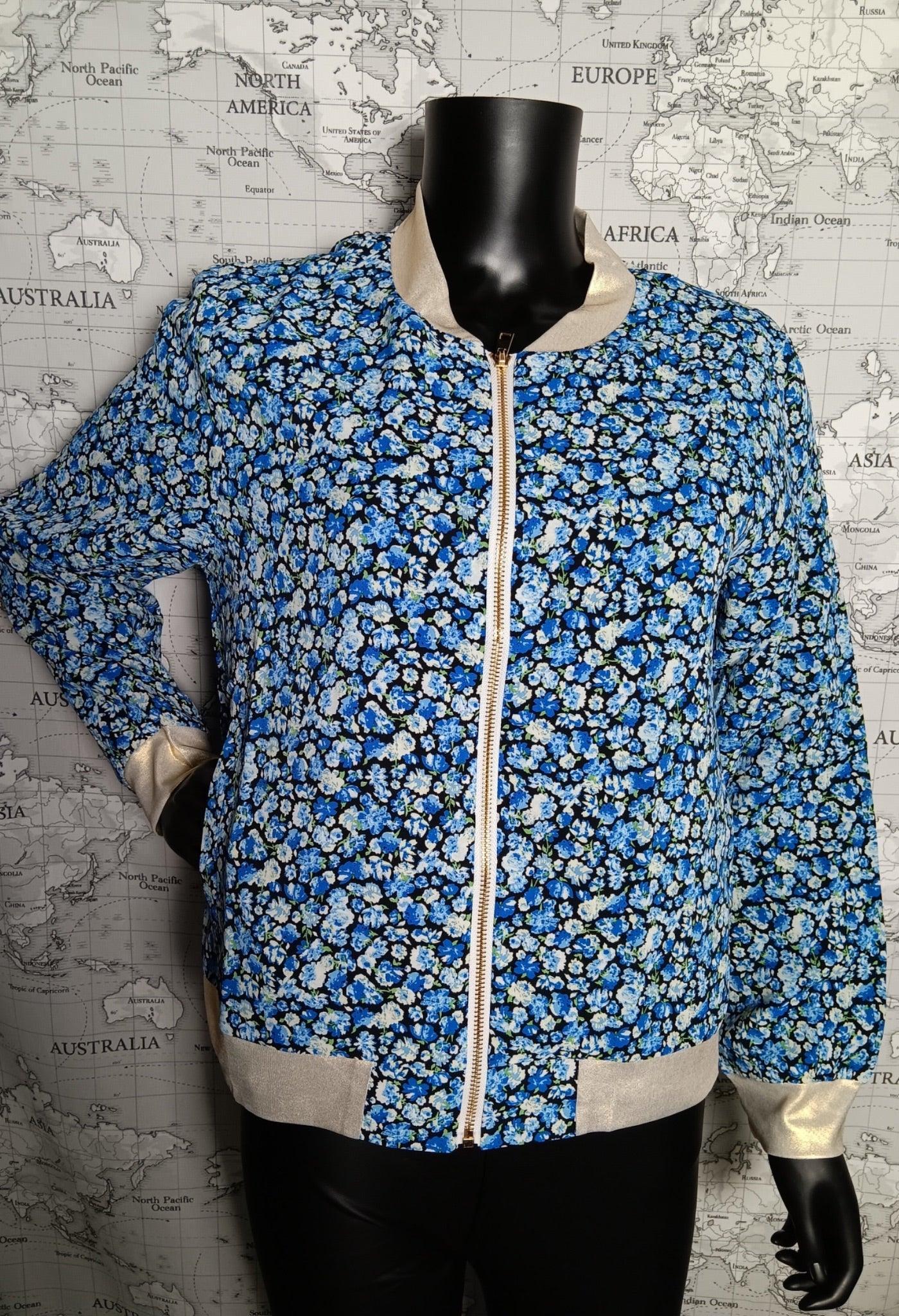 Veste bomber fleuri bleu à motifs petits bouquets blancs et noirs sur fond bleu, zip blanc et ourlets beige clair sur mannequin.
