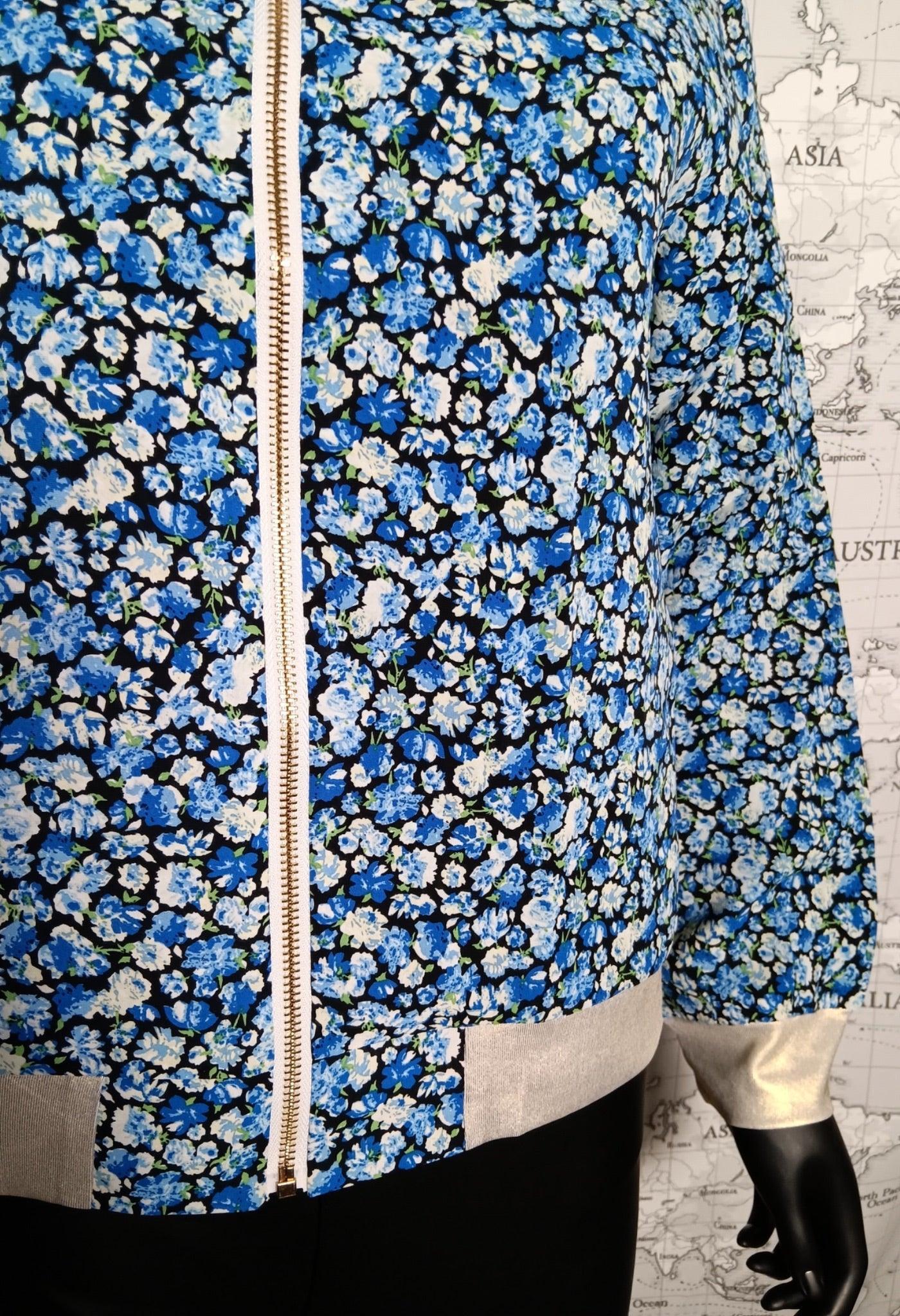 Bomber fleuri bleu et blanc, fermeture éclair métallique centrale, manches et ourlets gris clair, porté sur un mannequin.