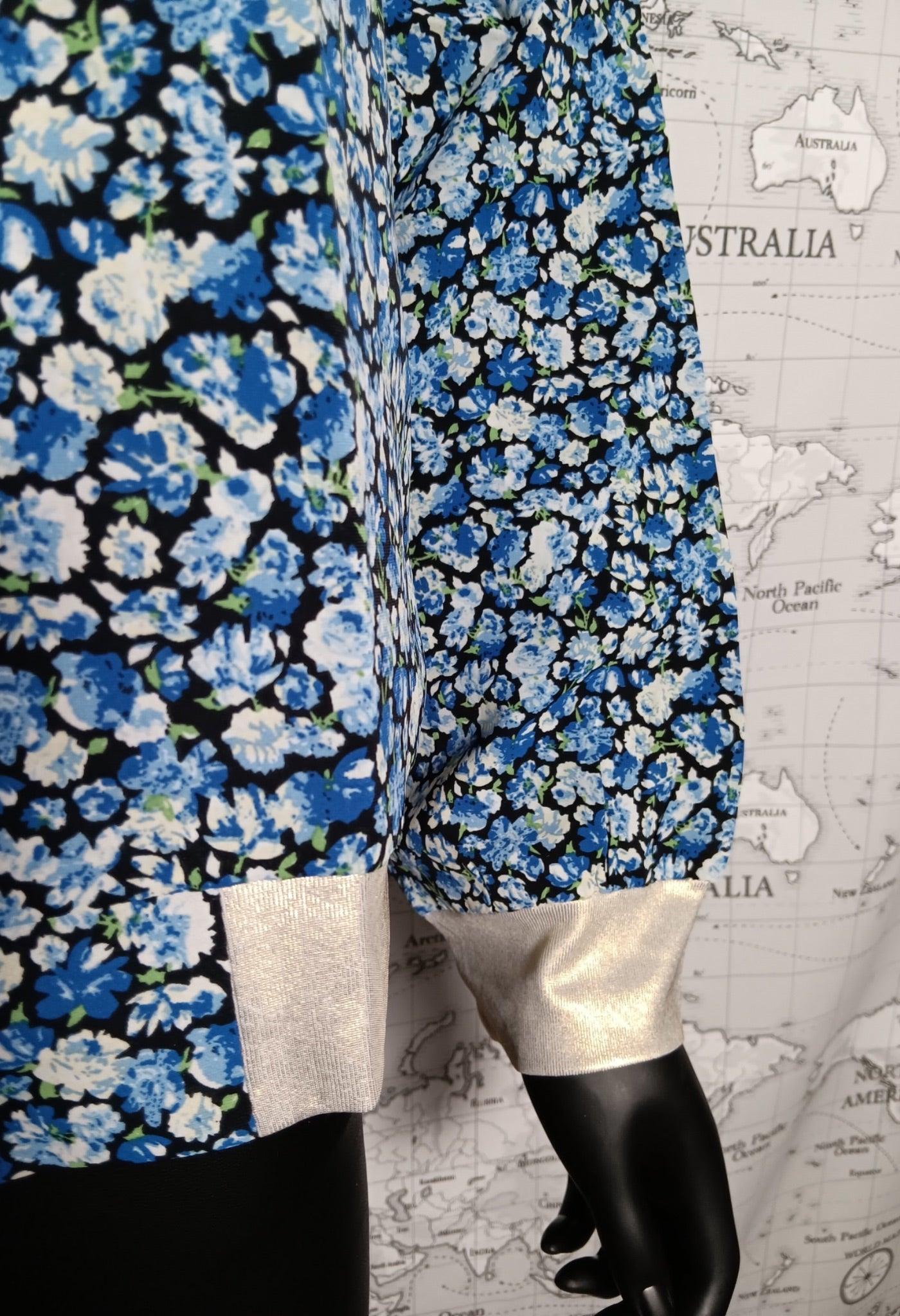 Mannequin portant une robe/chemise à fleurs bleues avec poignets et ourlet dorés, sur fond carte. Produit: Bomber fleuri femme tons de bleus - Le Petit Placard