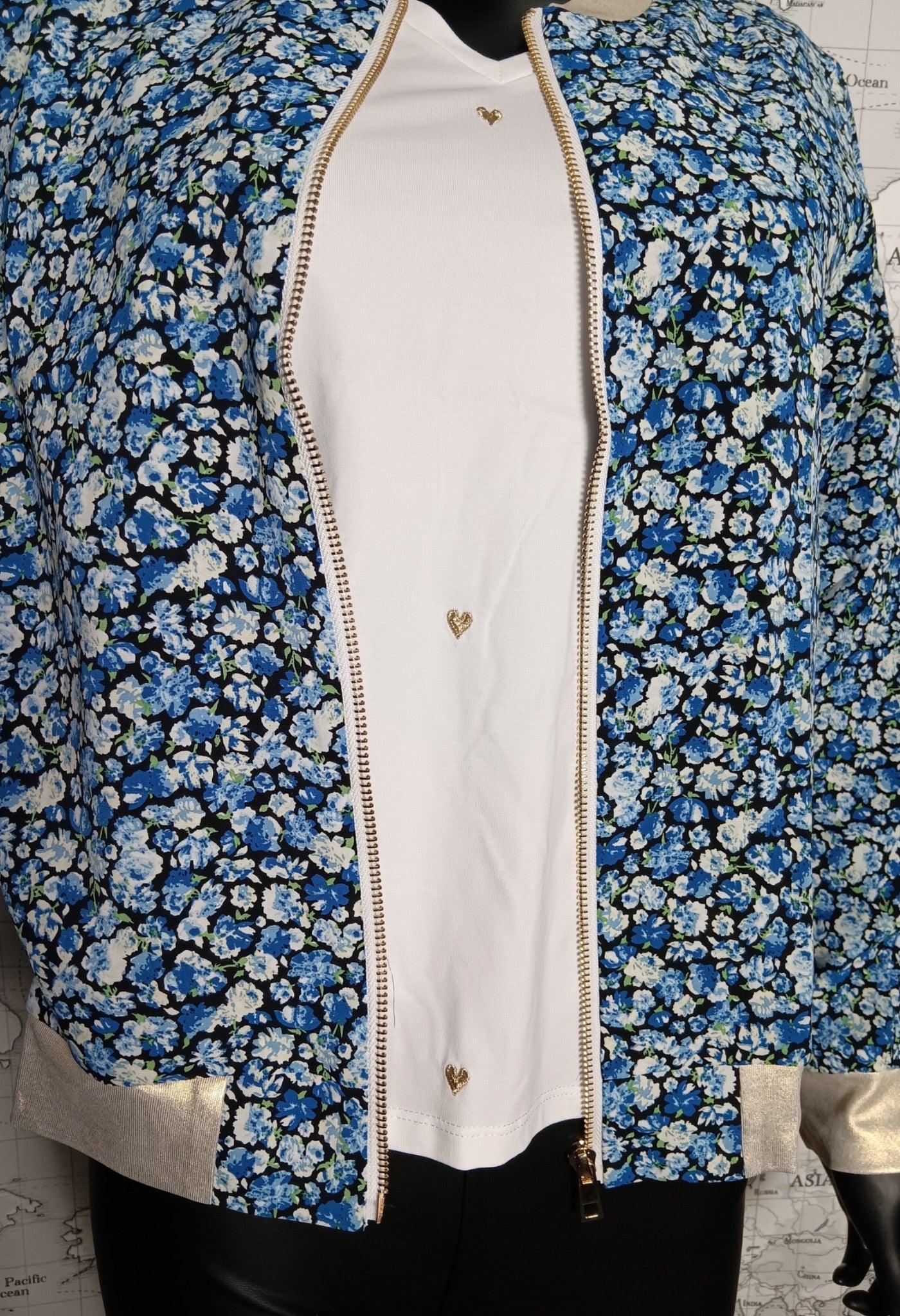 Veste bomber fleuri femme bleu, ouverte sur un top blanc, fermeture zippée dorée et détails dorés aux manches.