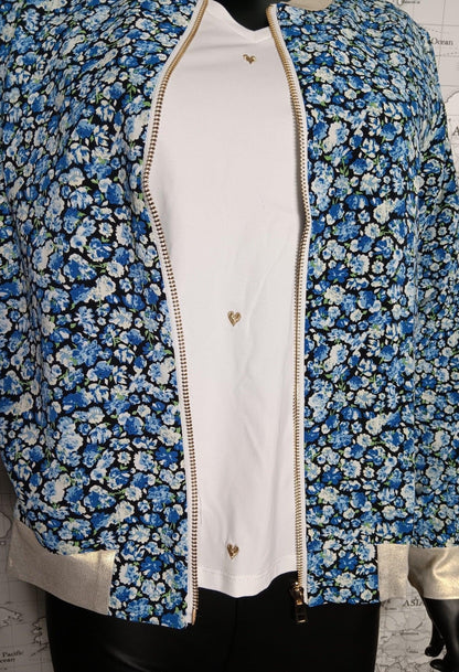 Veste bomber fleuri femme bleu, ouverte sur un top blanc, fermeture zippée dorée et détails dorés aux manches.