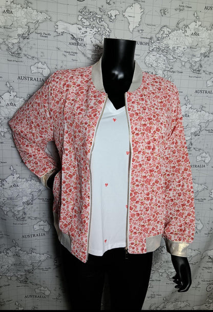 Veste bomber rose à motifs floraux rouges et blancs, livrée avec bordures crème et zip doré, portée sur mannequin noir près d’un mur décor imprimé carte du monde. Bombers Fleuri Rouge Orangé – Veste Femme Légère & Romantique.