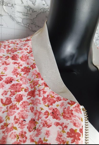 Veste légère romantique à imprimé fleuri rose et blanc avec bord-côte beige et fermeture éclair dorée, sur mannequin noir.