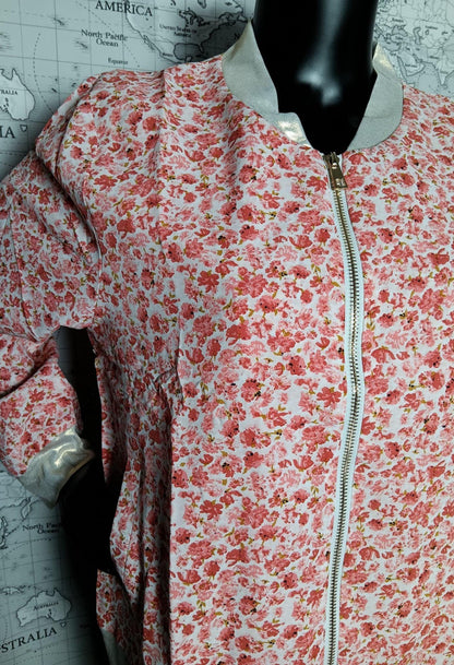 Veste bomber fleurie rouge et orangé légère pour femme, fermeture zippée centrale, motif floral sur fond clair, mannequin en carte du monde en arrière-plan.
