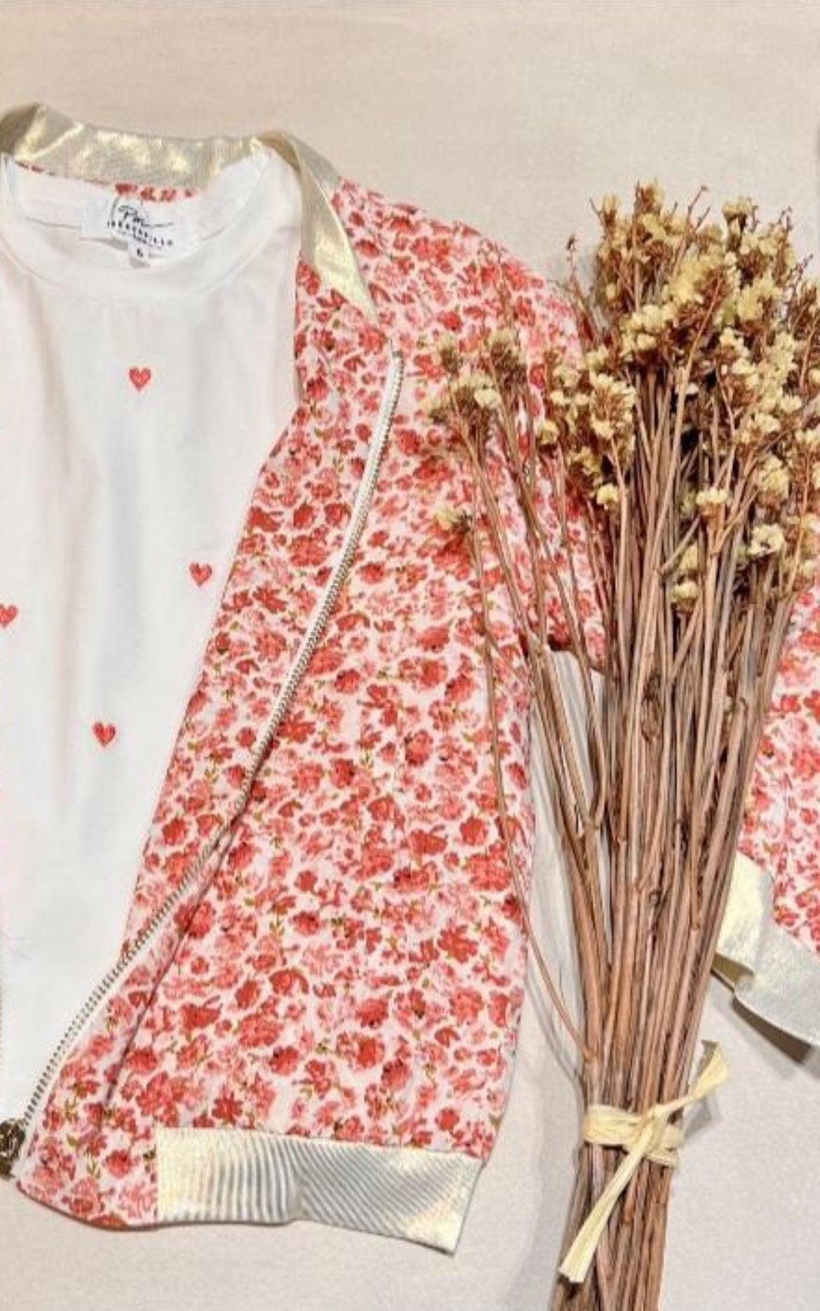 Veste légère fleurie rouge-orangé Bombers Fleuri Rouge Orangé, ouverte sur un t-shirt blanc à petits cœurs, près d’un bouquet de tiges séchées.