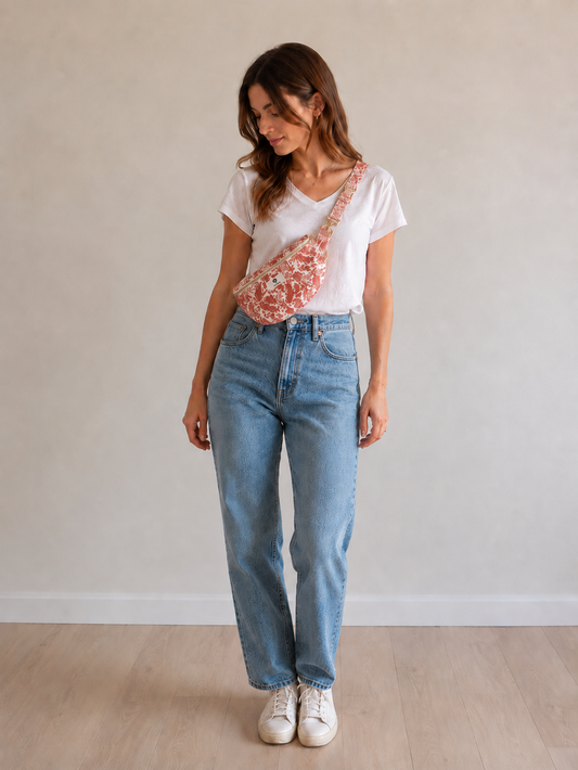 Sac banane femme en coton fleuri corail portée en diagonal sur le torse, avec t-shirt blanc et jean bleu.