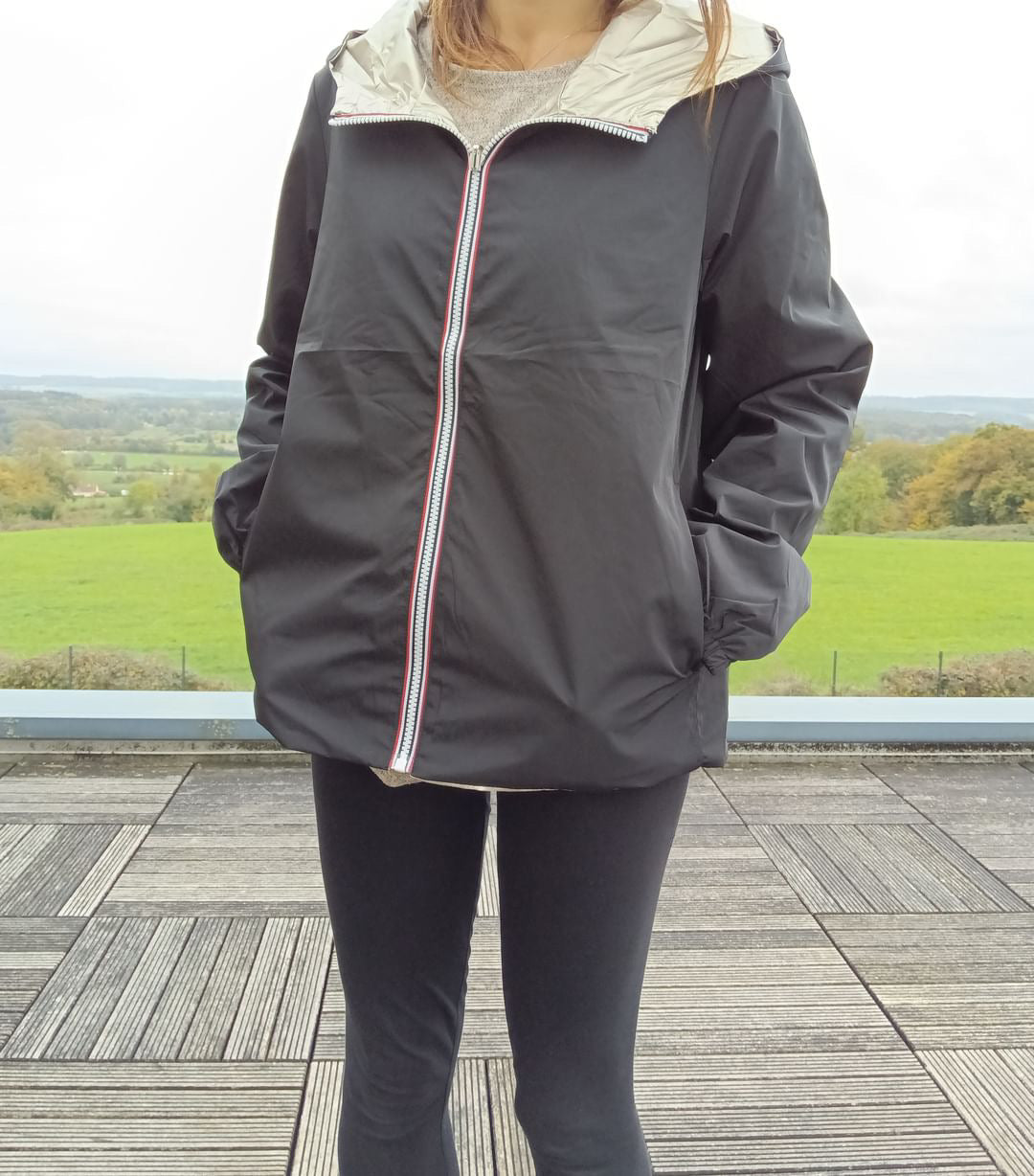 Manteau court réversible imperméable noir porté côté noir, avec capuche dorée visible et fermeture éclair bicolore – Melya Melody