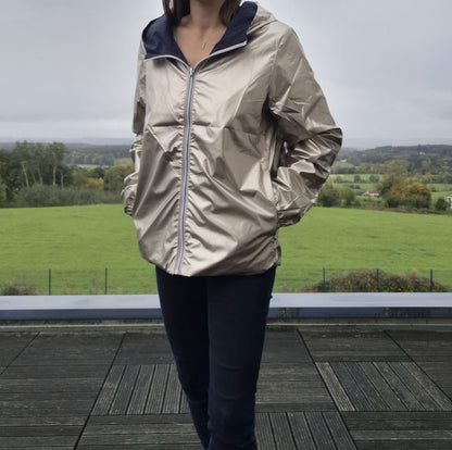 Manteau court imperméable réversible doré Melya Melody porté côté doré, avec capuche bleu marine, sur terrasse en bois