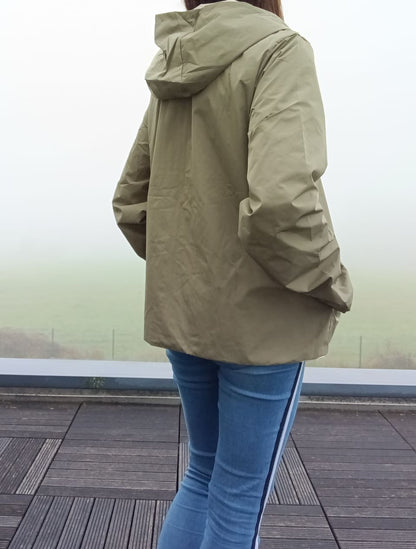 Femme de dos portant le manteau court léger imperméable kaki réversible Melya Melody à capuche, par temps brumeux