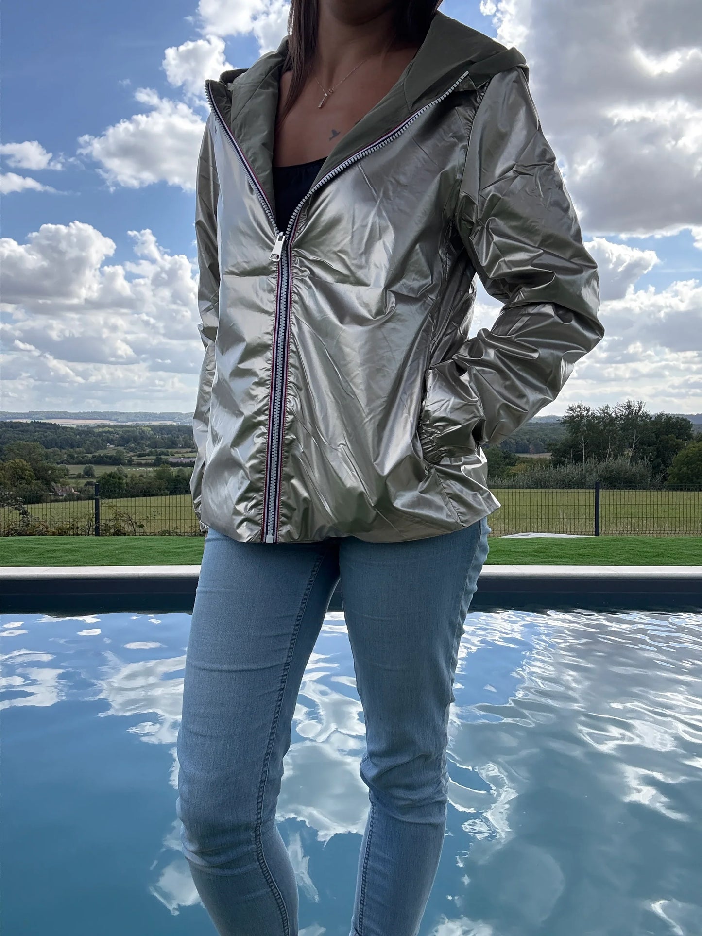 Manteau court léger imperméable kaki réversible doré Melya Melody porté avec un jean, vue extérieure près d'une piscine