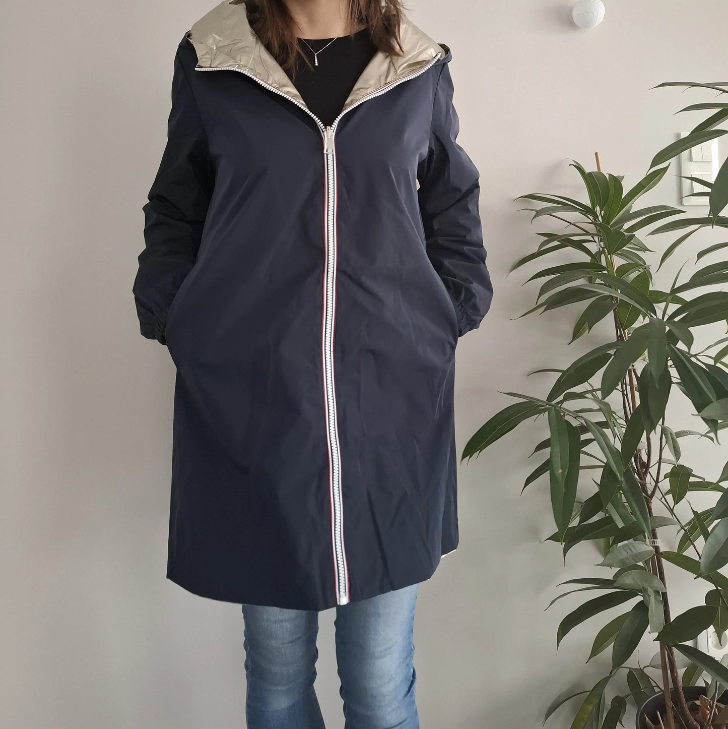 Woman wearing a navy Laura Jo raincoat from Le Petit Placard, standing indoors near a plant