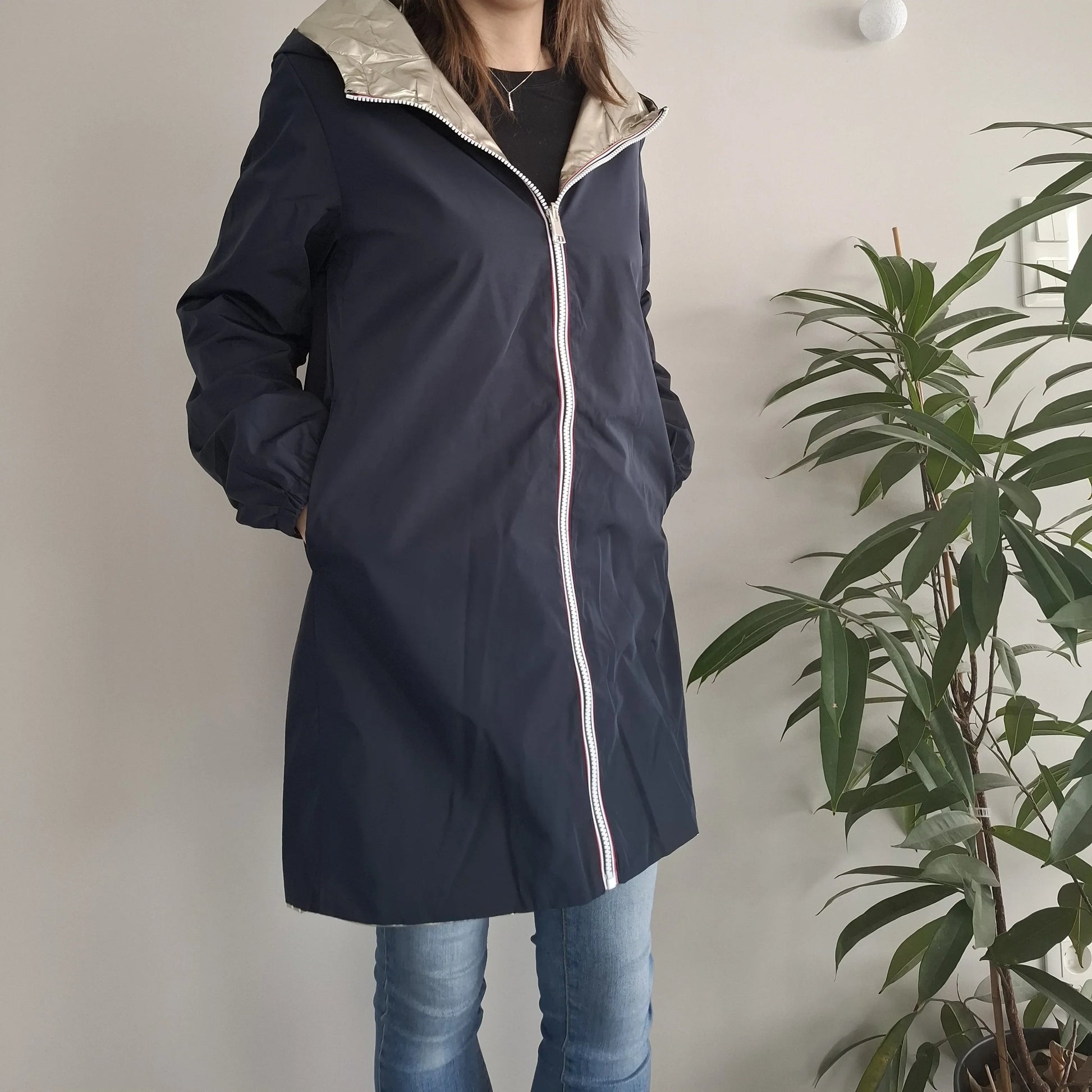 Woman wearing a Laura Jo navy raincoat with silver hood, standing indoors by a plant