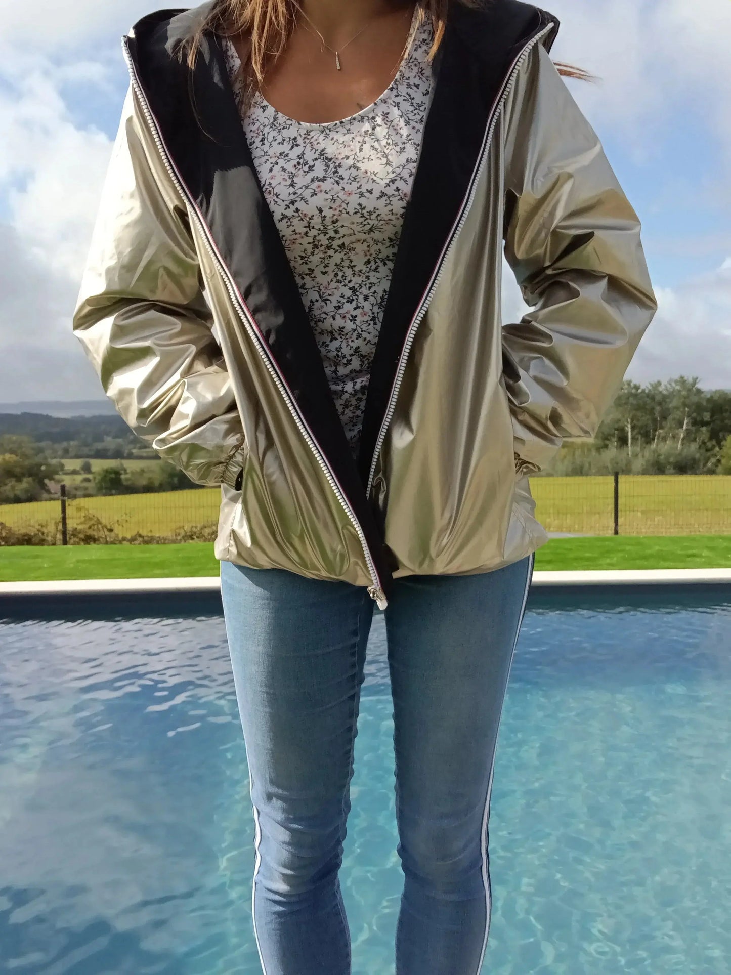 Manteau court réversible imperméable noir et doré Melya Melody, porté sur un mannequin avec capuche et fermeture éclair visible.