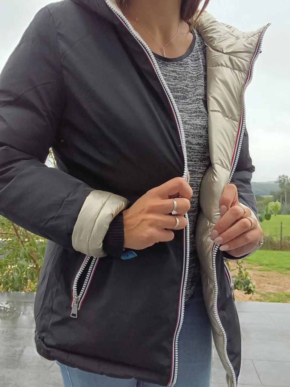 Manteau court réversible Melya Melody, imperméable et matelassé noir et doré, porté avec capuche et fermeture éclair.