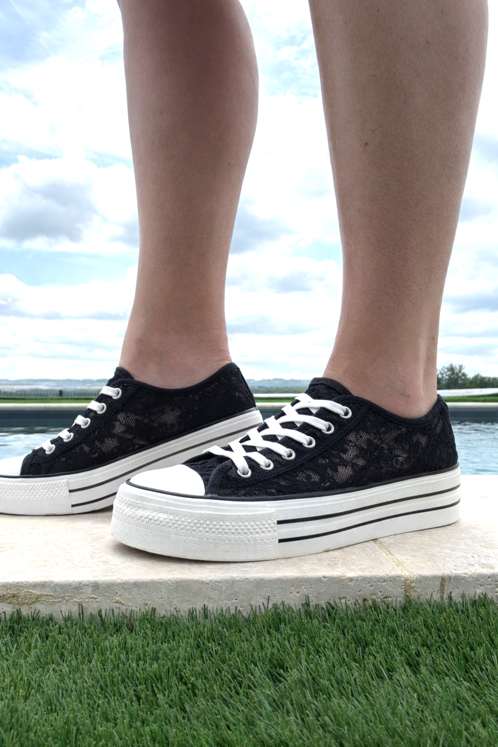 Basket Plateforme Dentelle Noire Femme avec semelle épaisse: pieds portant des tennis noires en dentelle, lacets blancs, grande semelle blanche à rayures noires.
