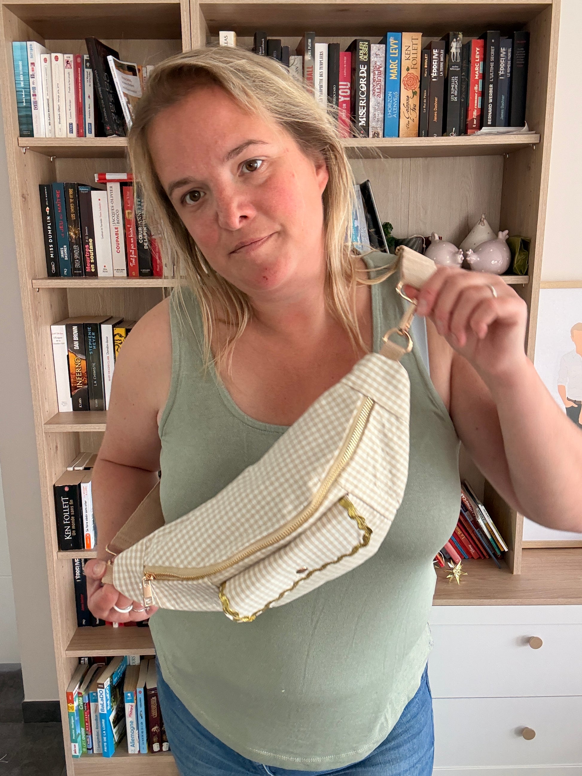 Sac banane en tissu vichy beige et blanc tenu à deux mains, détail bordure dorée et poche avant