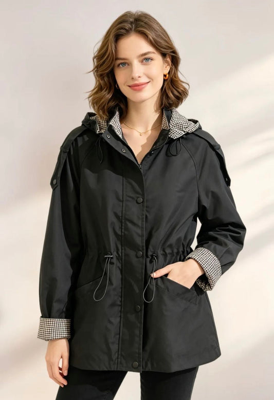 Veste de pluie noire femme avec capuche intégrée, intérieur pied-de-poule, coupe cintrée et cordon de serrage.